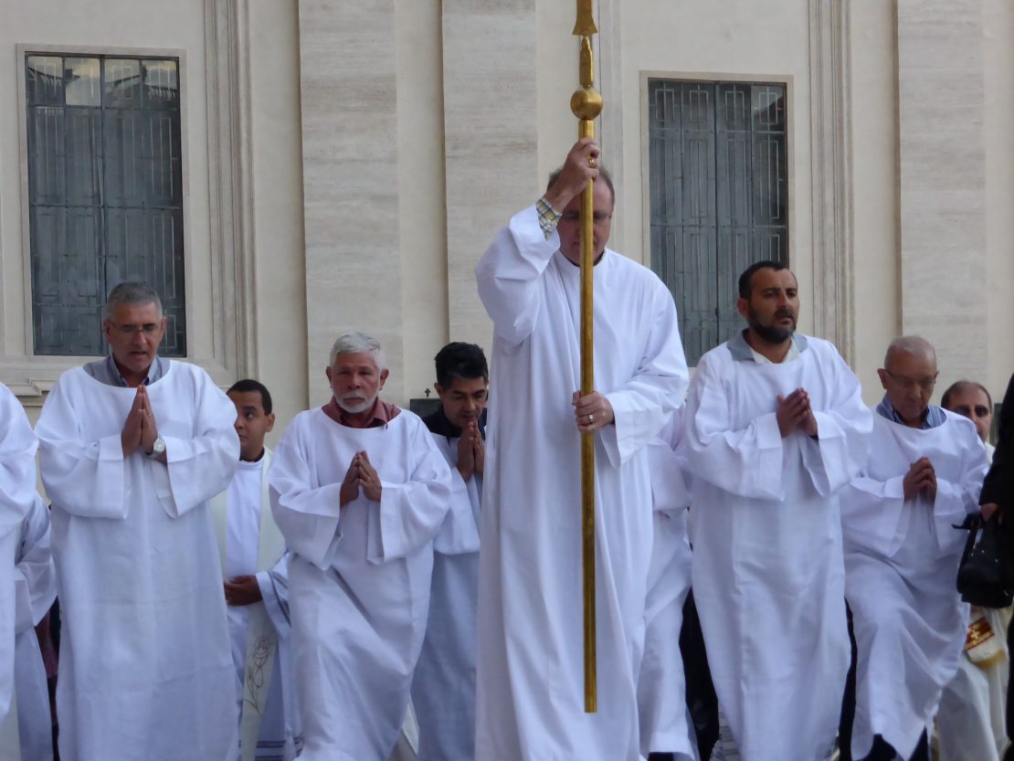 Man in white robe carrying staff leads procession into St. Peter's Basilica