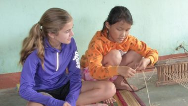 Vietnamese girl teaches American girl how to weave mats
